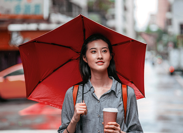 Female traveler holding umbrella and coffee cup