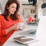 Independent travel advisor looking at laptop holding a coffee cup
