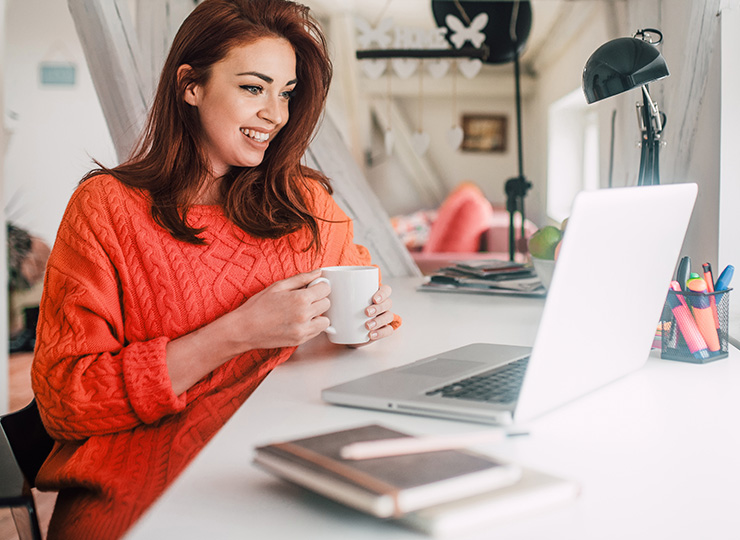 Independent travel advisor looking at laptop holding a coffee cup