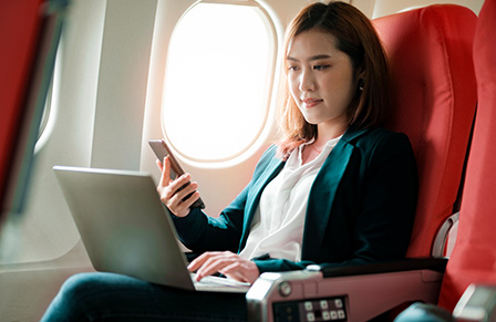 Host agency - female traveler on plane reading the 1000 Mile Travel Group website on her laptop